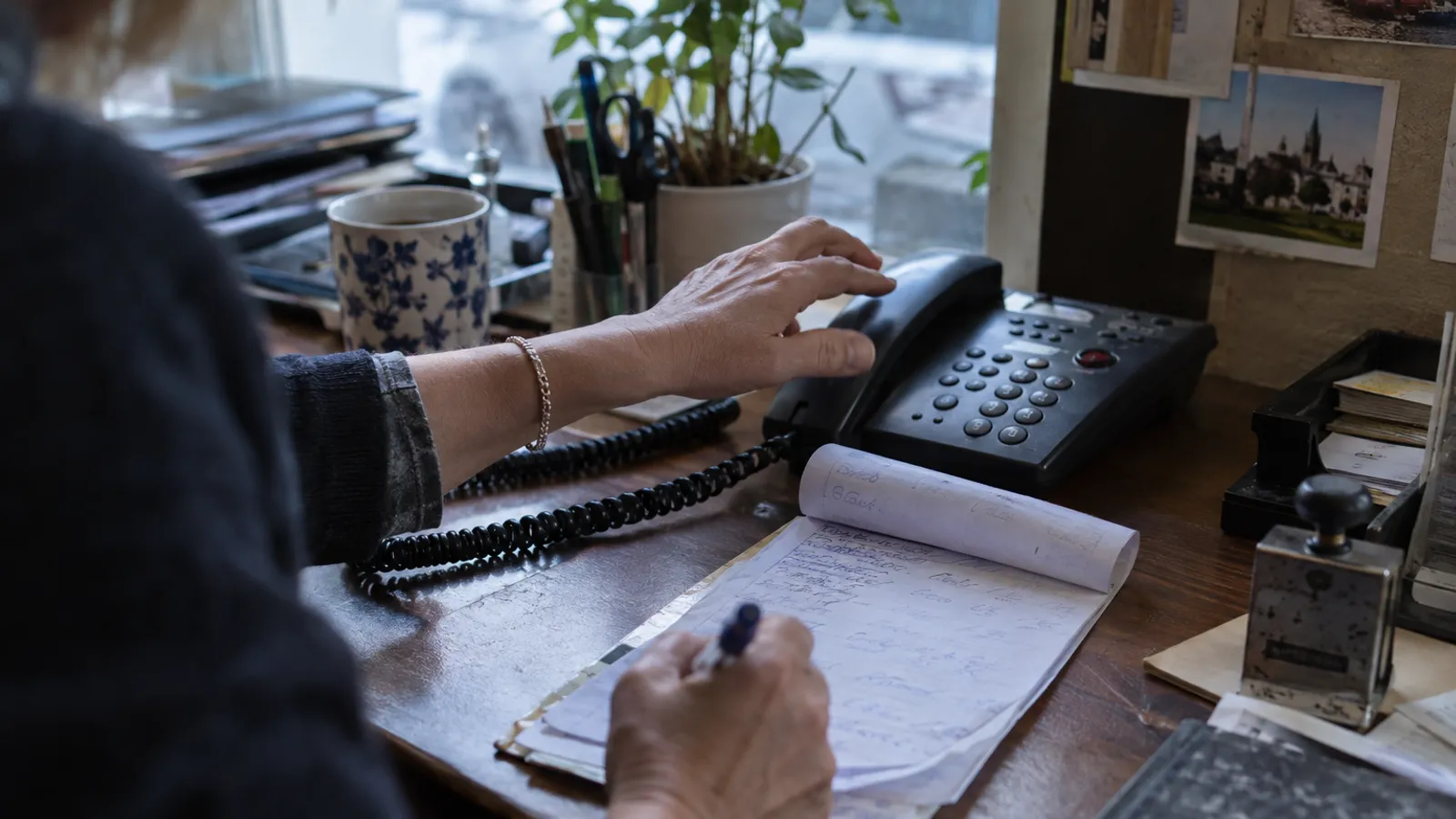 Ein klingelndes Bürotelefon neben einer handschriftlichen Rückrufliste, eine Hand greift zum Hörer.